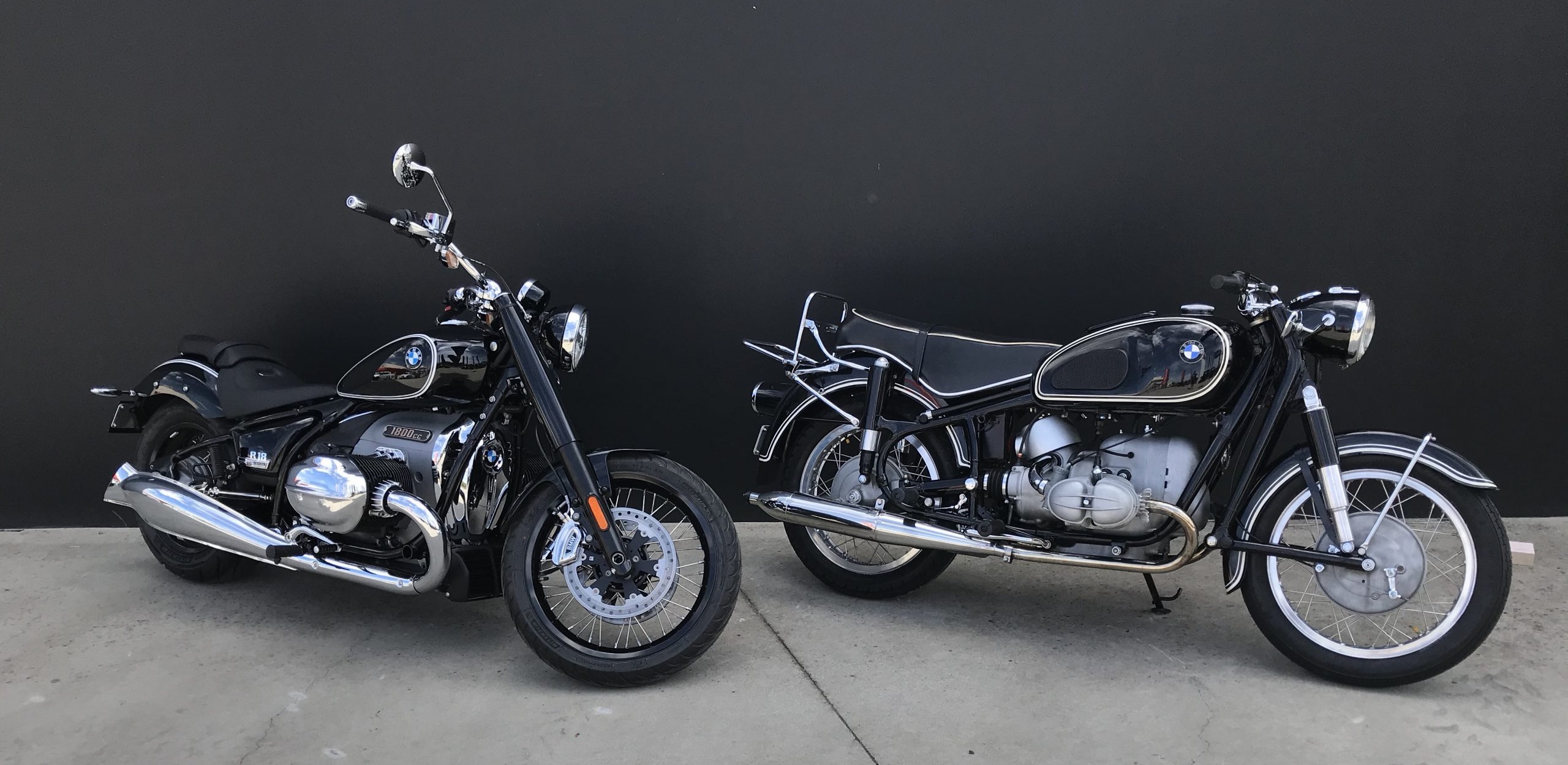 A BMW R 18 parked beside a 1950s BMW boxer twin in front of the Munich Motorcycles showroom wall